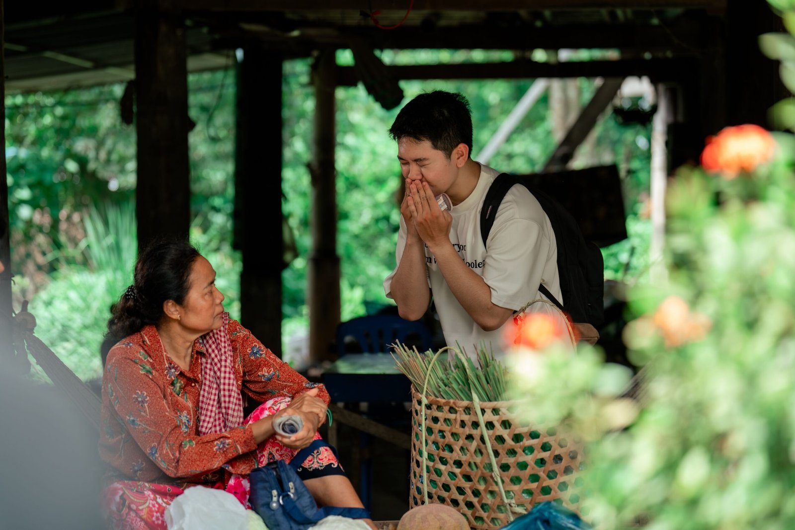 A warm interaction between two people in an outdoor market setting, surrounded by greenery.